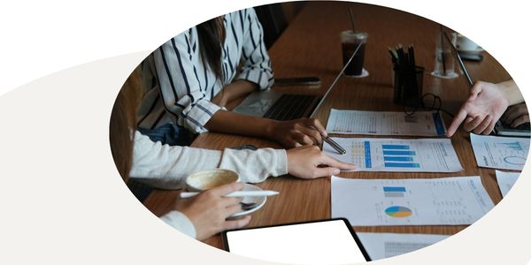 Graphic of three people, one with a laptop, looking at charts on a table, in a circular frame with a white and tan background.
