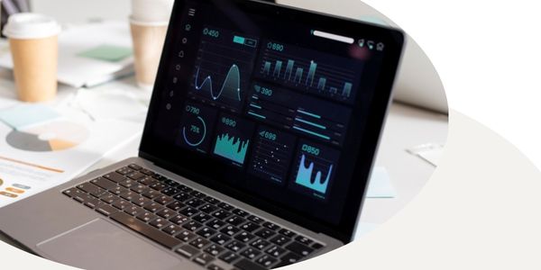Laptop on a desk showing a screen with graphs and charts, in a circular frame with a white and tan background.